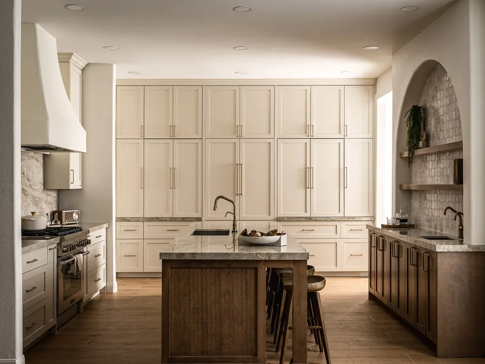 Remodeled Breakaway kitchen with cream custom cabinetry, a walnut island with seating, a plaster range hood and a stone worktop.
